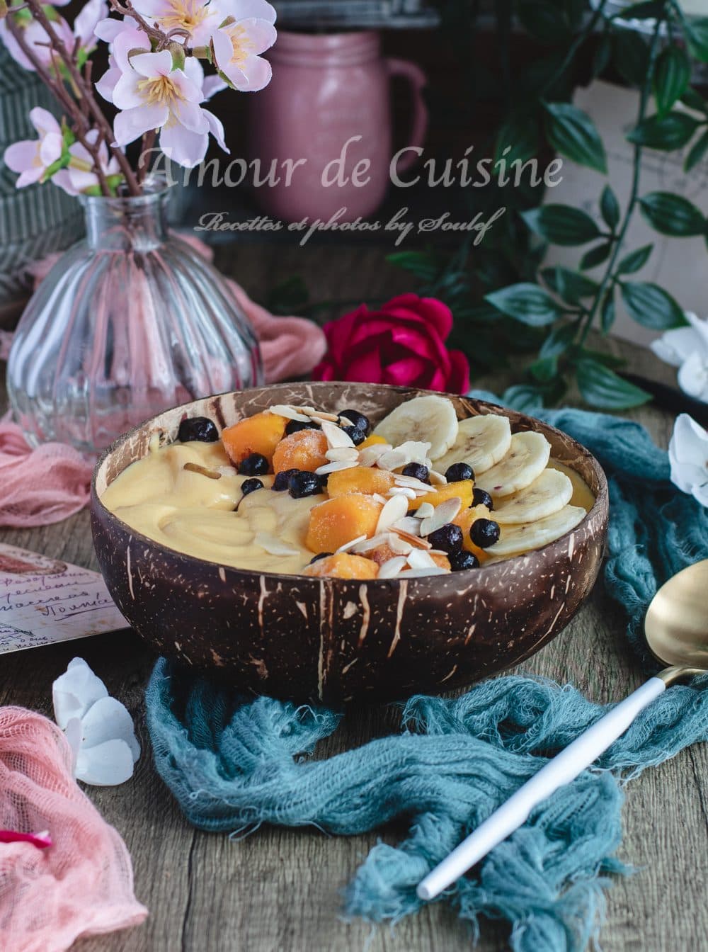 Creamy mango banana smoothie bowl in a coconut bowl, topped with banana slices, mango chunks, blueberries, and flaked almonds, set on a rustic table with a spoon.