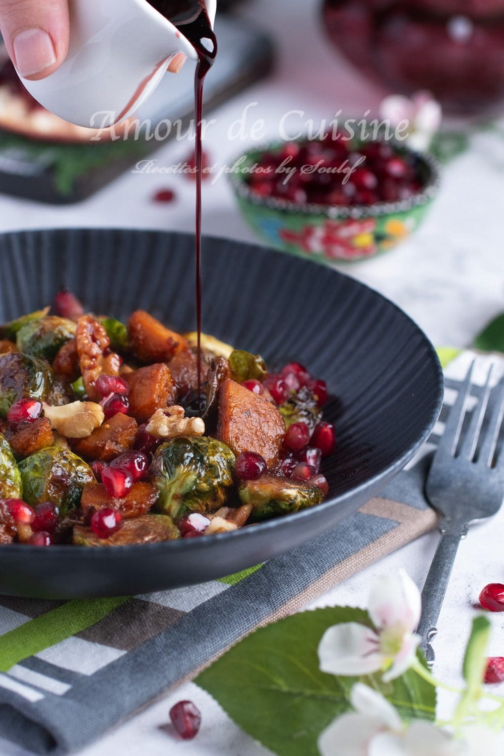 Pomegranate molasses being poured over a dish of roasted Brussels sprouts and pumpkin, topped with nuts and pomegranate seeds, a colorful, indulgent plate perfect for a festive winter meal.