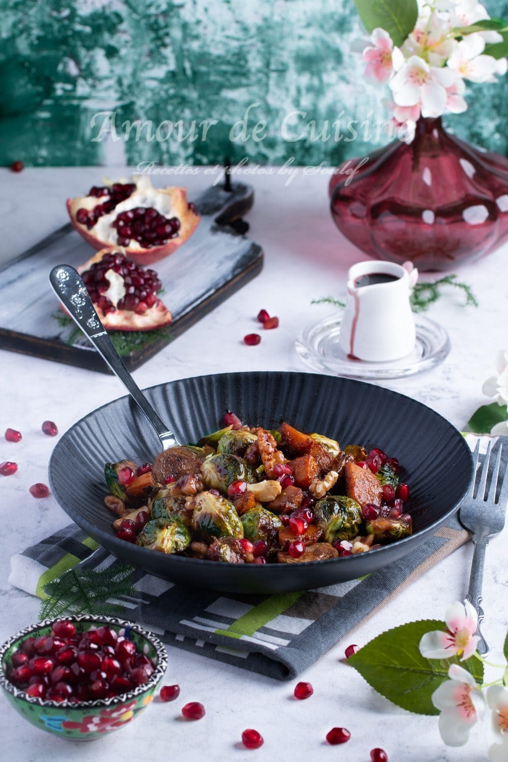 Plate of roasted Brussels sprouts and pumpkin with pomegranate molasses, topped with nuts and pomegranate seeds, presented on a flower- and fruit-decorated table for a colorful, festive, and indulgent meal.