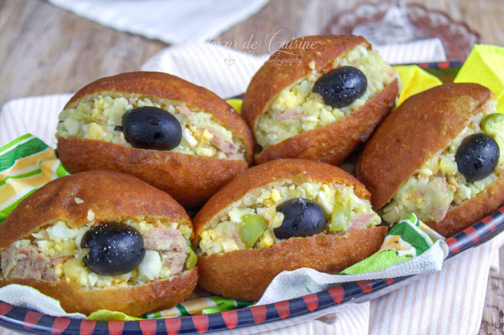 Plateau de fricassés tunisiens maison, petits pains frits bien dorés, garnis de thon, pomme de terre et œuf, avec une olive noire sur chaque sandwich