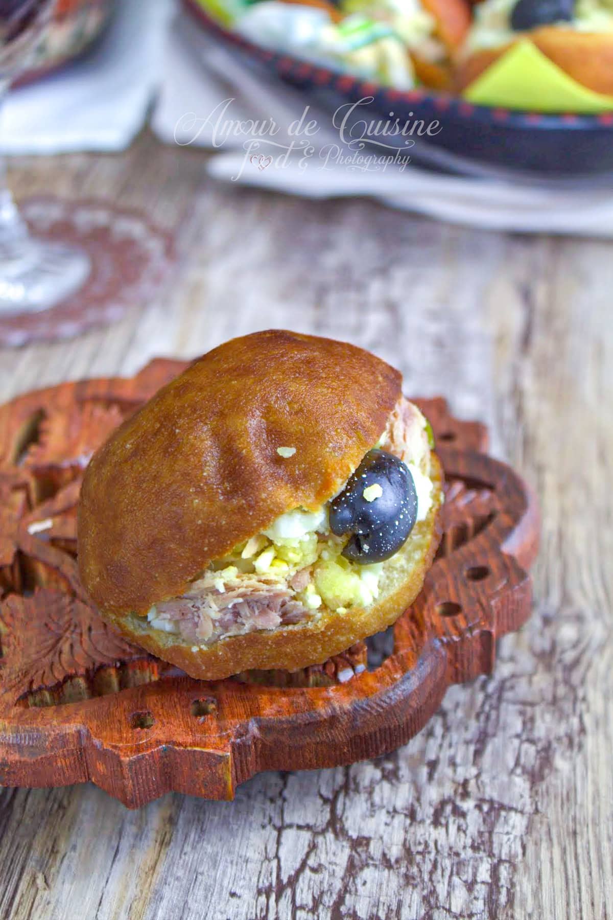 Fricassé tunisien doré servi sur une planche en bois, garni de thon, pomme de terre et œuf, avec une olive noire sur le dessus.