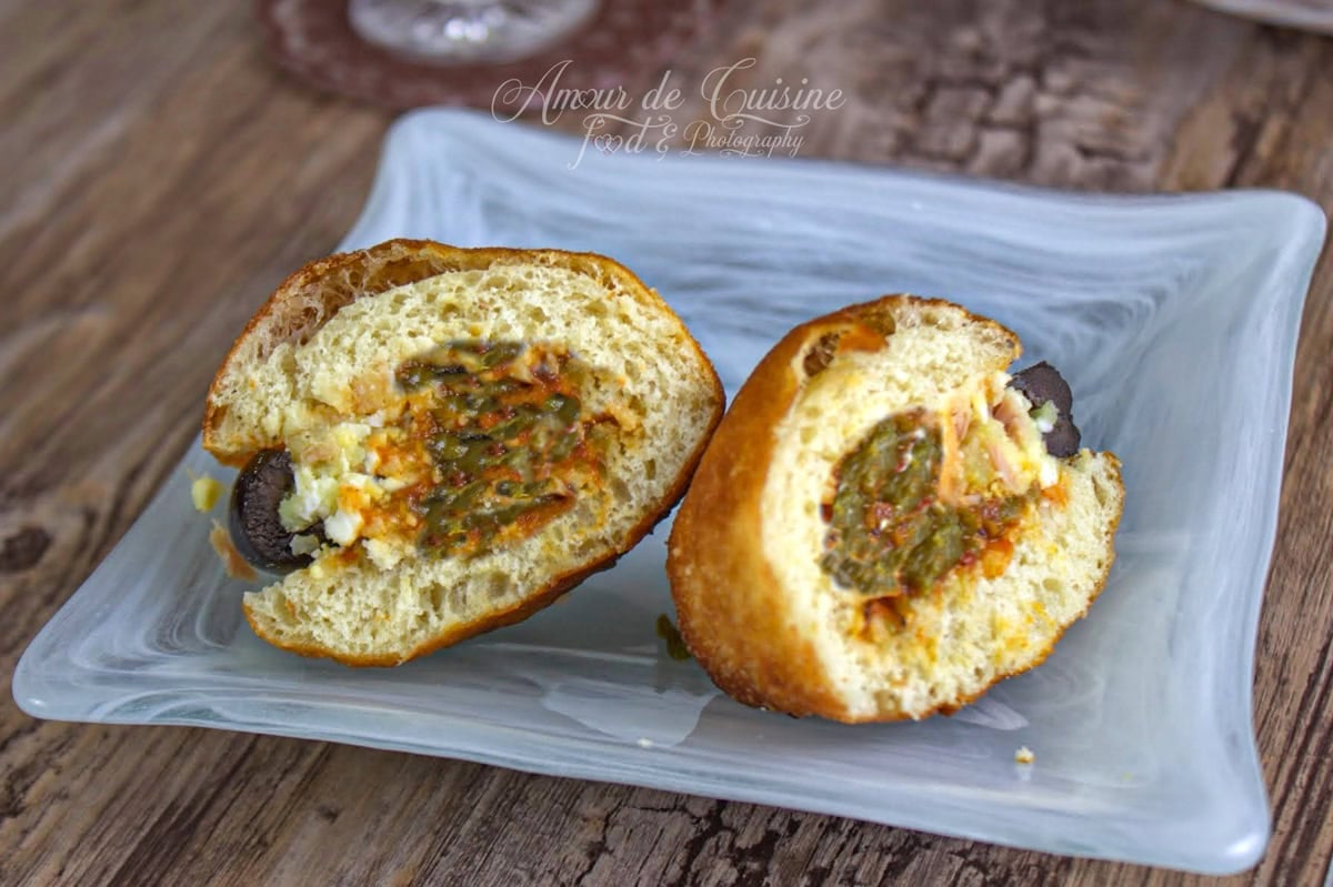 Fricassé tunisien coupé en deux sur une assiette, montrant la mie moelleuse et la garniture au hmiss, thon et olives.