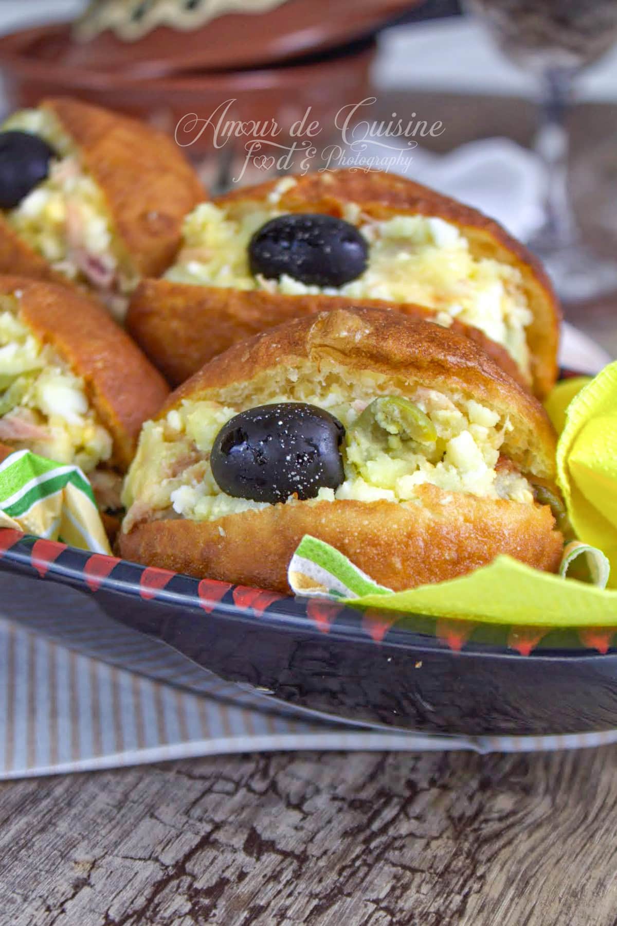 Fricassés tunisiens dorés, petits pains frits garnis de thon, pomme de terre et œuf, décorés d’une olive noire, servis dans un plat