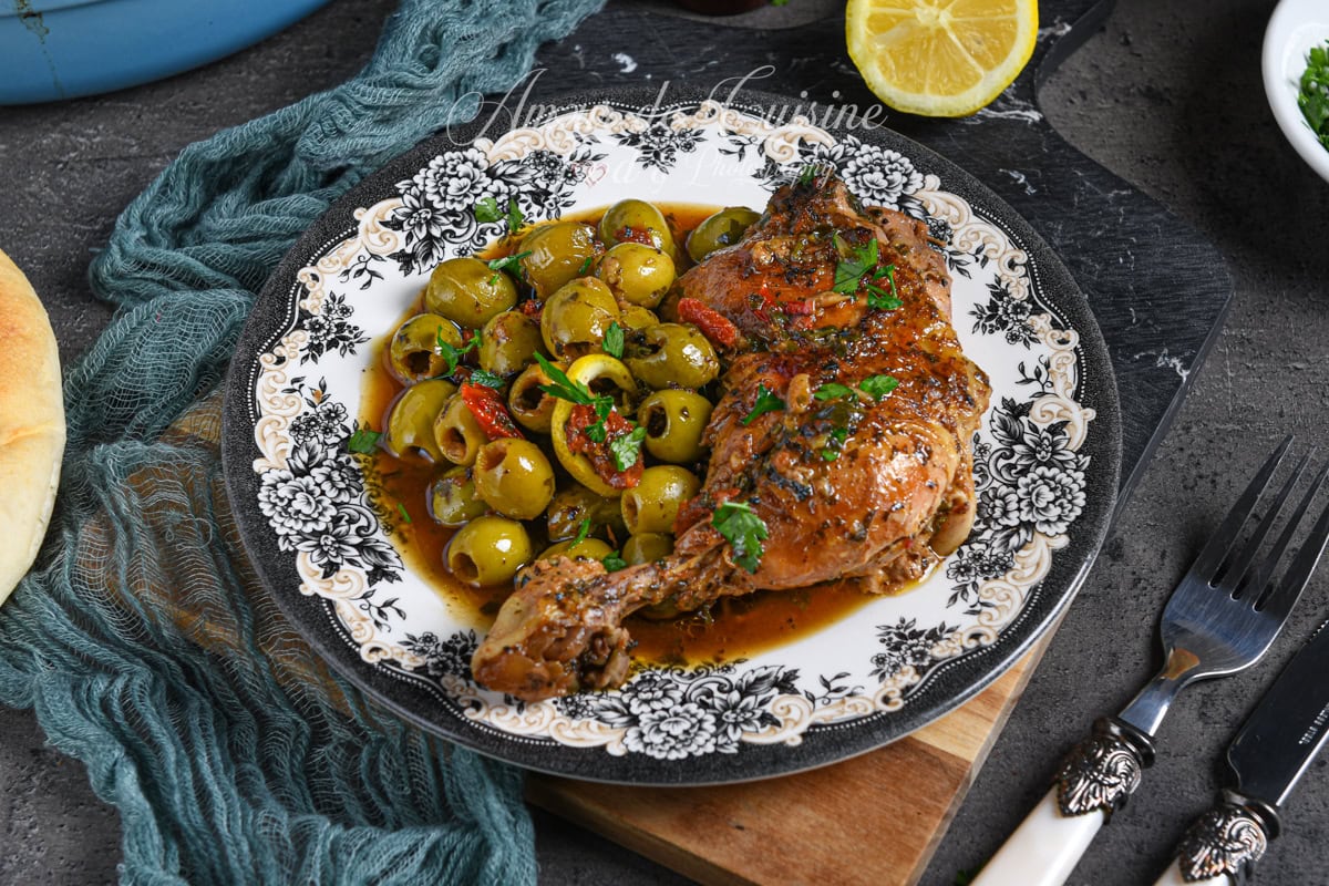 Assiette de tajine de poulet aux olives vertes et tomates séchées, nappé de sauce parfumée, garni de persil frais et rondelles de citron, servie avec pain maison.