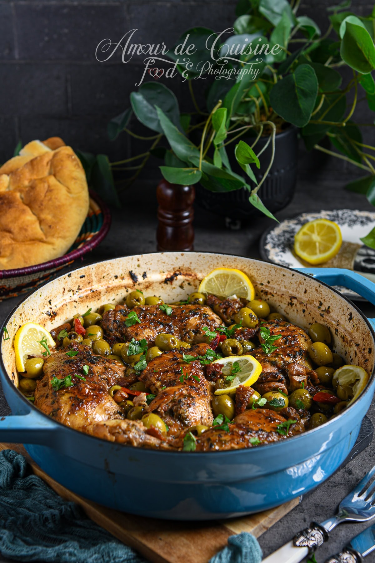 Cocotte bleue remplie de tajine de poulet aux olives vertes, tomates séchées et rondelles de citron, parsemé de coriandre fraîche, servie avec pain traditionnel.
