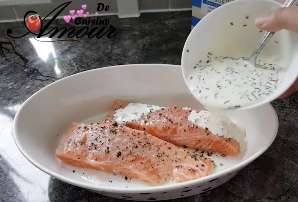 Fresh salmon fillets seasoned with black pepper in a baking dish, topped with creamy lemon and chive sauce before oven cooking
