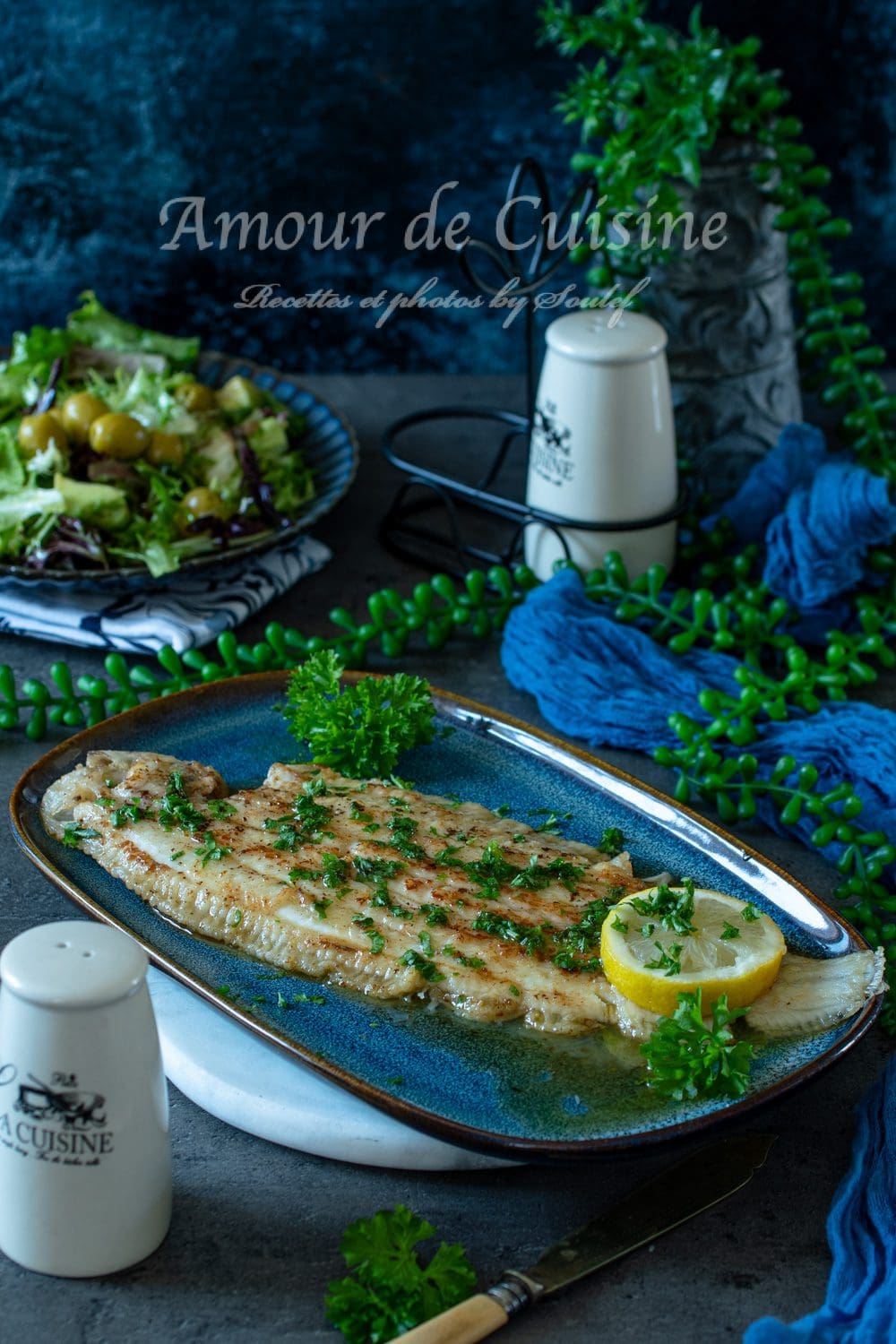 Sole meunière dorée au beurre noisette, citron et persil, servie sur une assiette bleue, avec une salade verte en arrière-plan et une table dressée dans une ambiance chaleureuse.