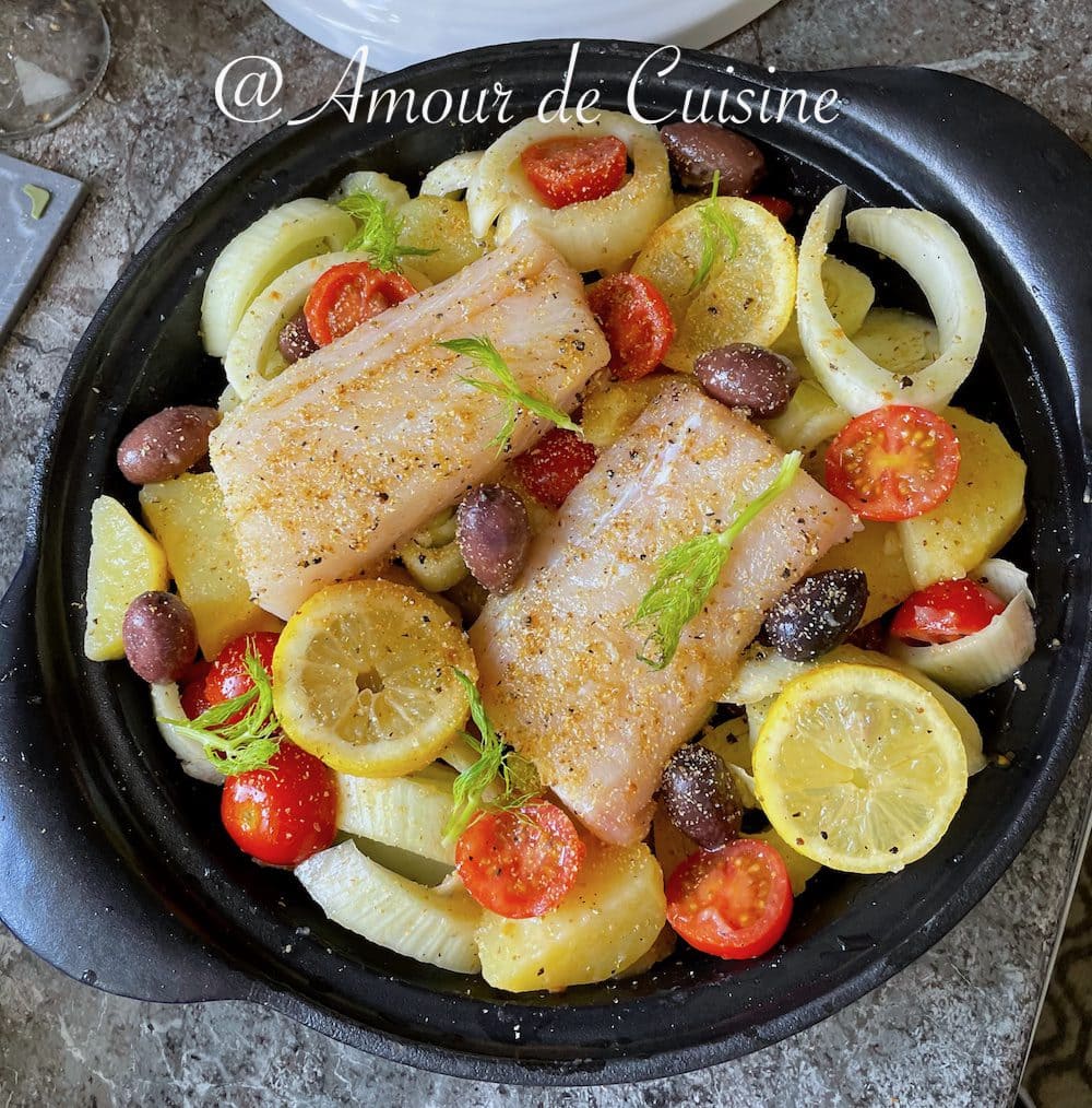Uncooked tagine made with raw haddock fillets, potato slices, fennel, lemons, cherry tomatoes, and black olives, beautifully arranged in a black ceramic dish, ready to go into the oven.