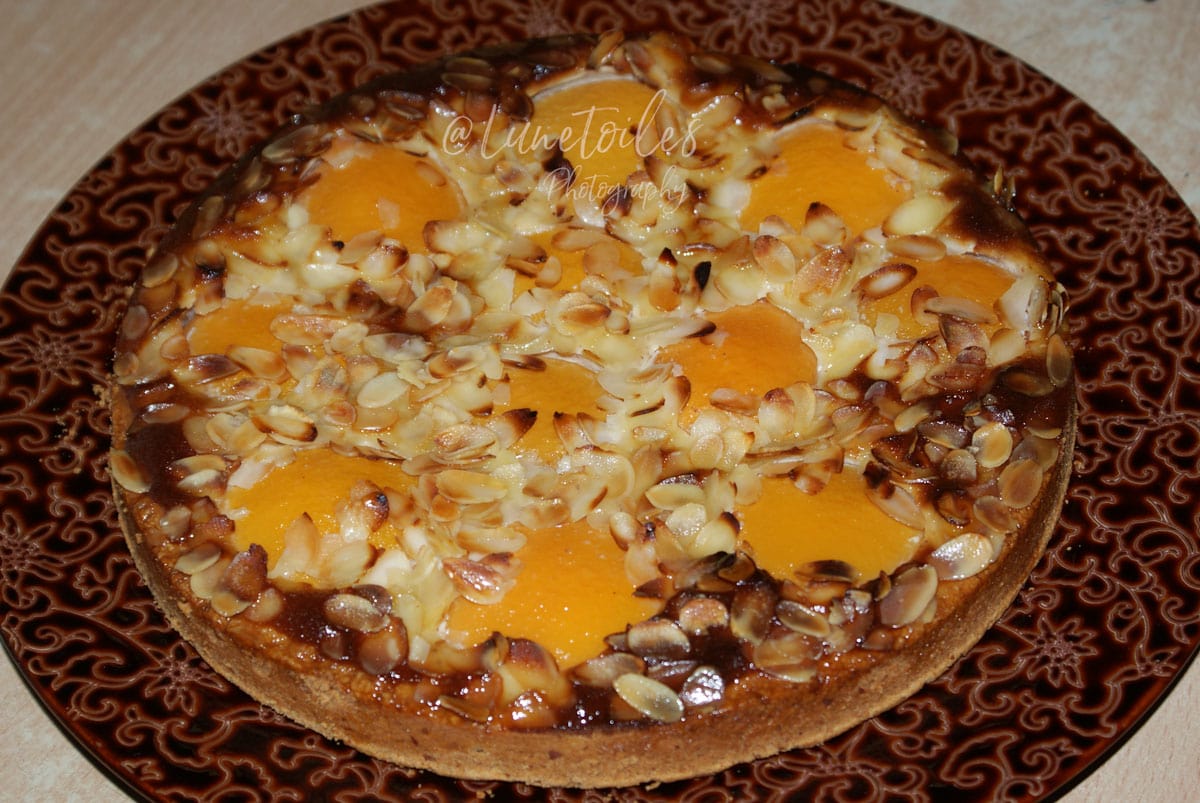 Tarte aux pêches amandine entière, décorée de demi-pêches au sirop, crème d’amande dorée et amandes effilées grillées.