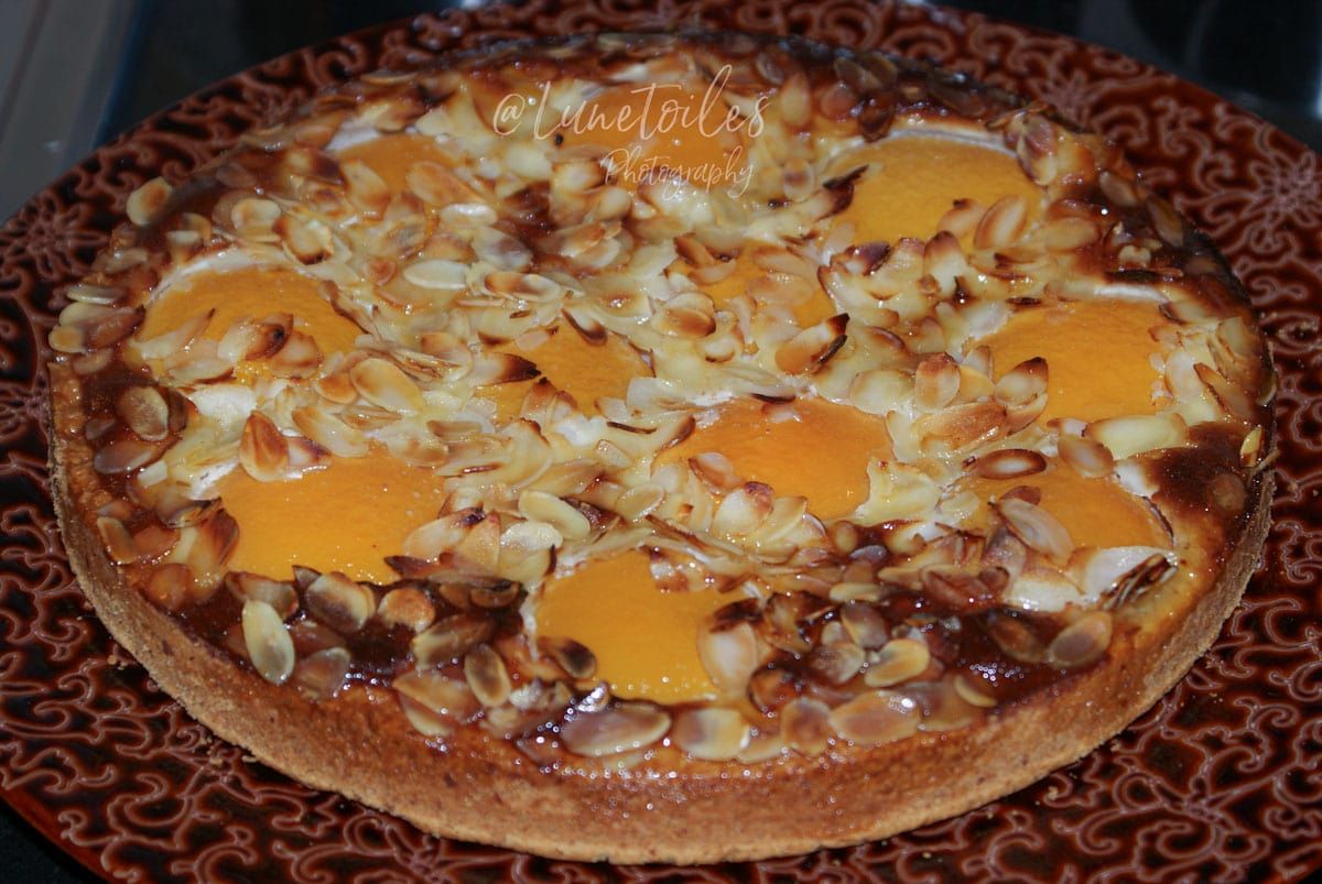 Tarte aux pêches amandine bien dorée, garnie de pêches au sirop, crème d’amande fondante et amandes effilées grillées.