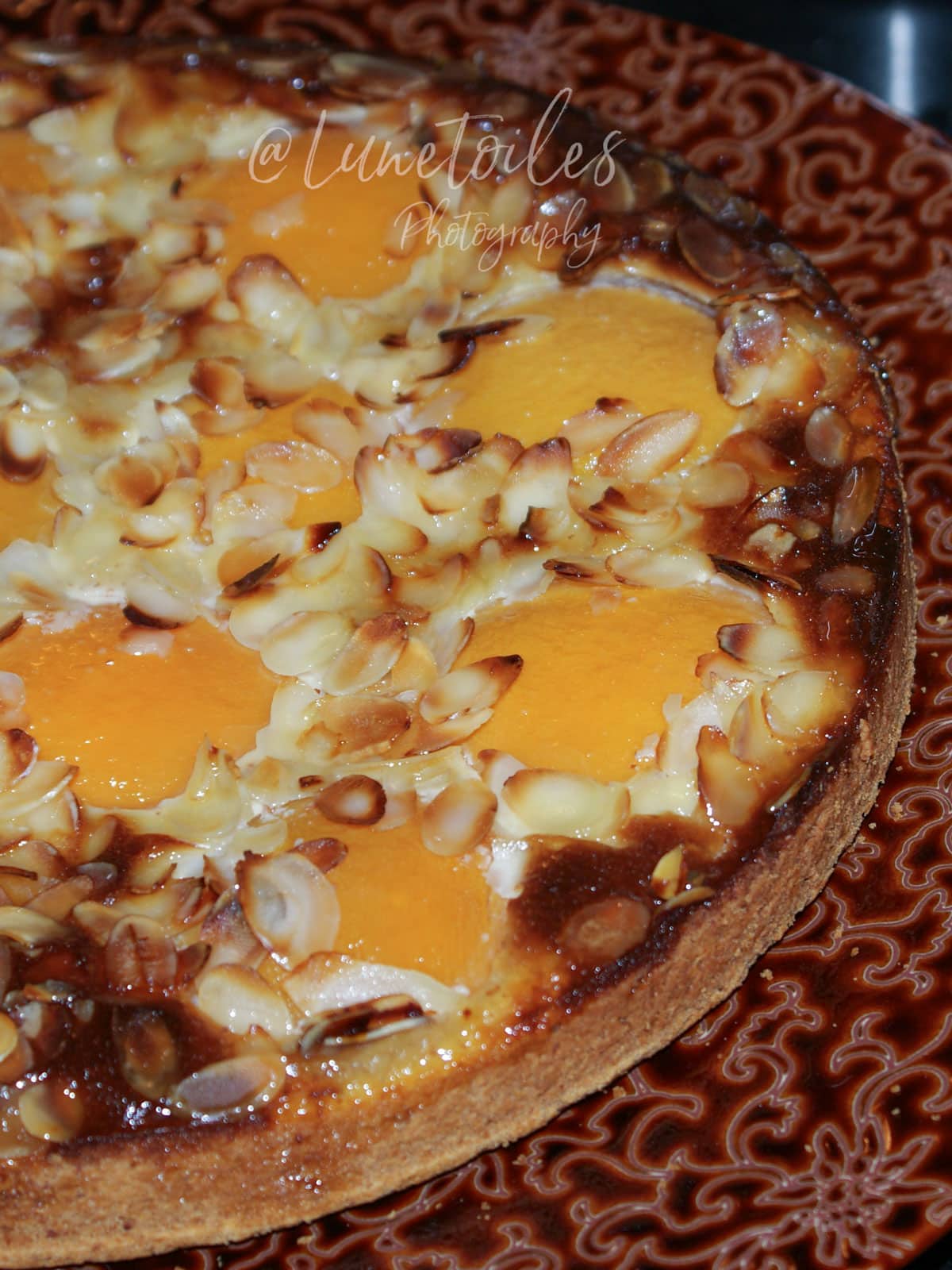 Tarte aux pêches amandine dorée, garnie de demi-pêches au sirop, crème d’amande fondante et amandes effilées grillées.