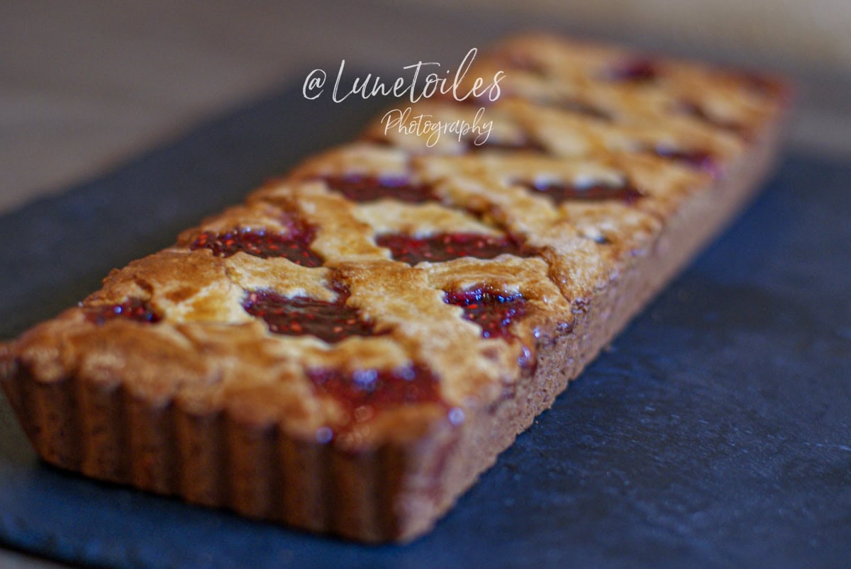 Linzer Torte rectangulaire cuite, à la croûte dorée et brillante, ornée de croisillons de pâte et de confiture de framboises, posée sur une ardoise noire, photographie signée @Lunetoiles