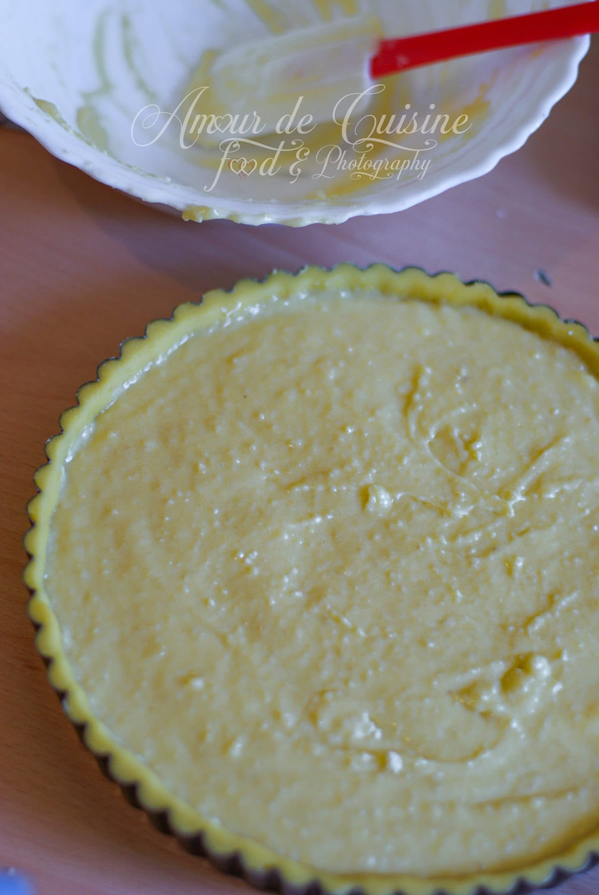Fond de tarte cannelé garni de frangipane (crème d’amandes) étalée en couche régulière, avec un bol et une spatule au-dessus sur le plan de travail.