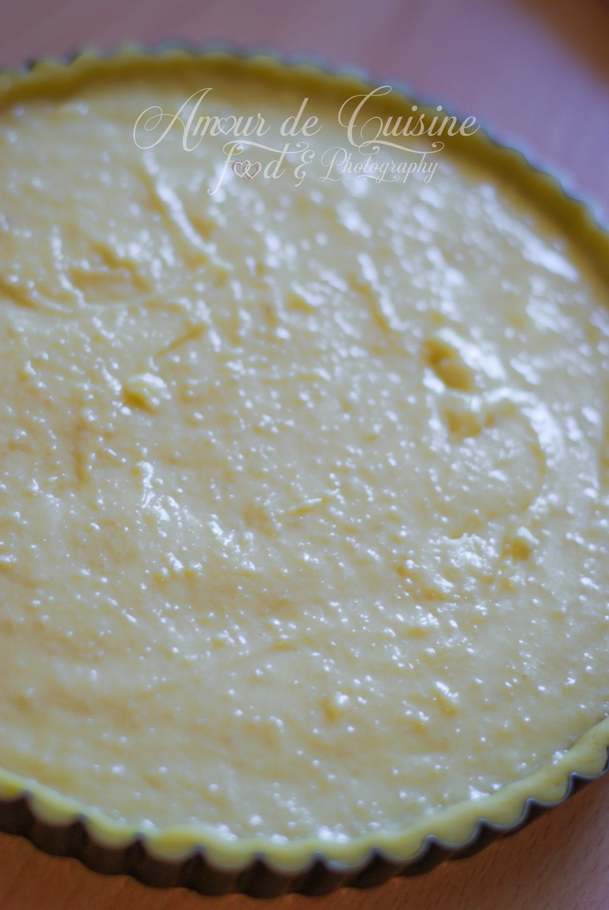 Gros plan sur un moule à tarte cannelé rempli de frangipane (crème d’amandes), étalée de façon irrégulière avant cuisson, avec une surface brillante et légèrement granuleuse.