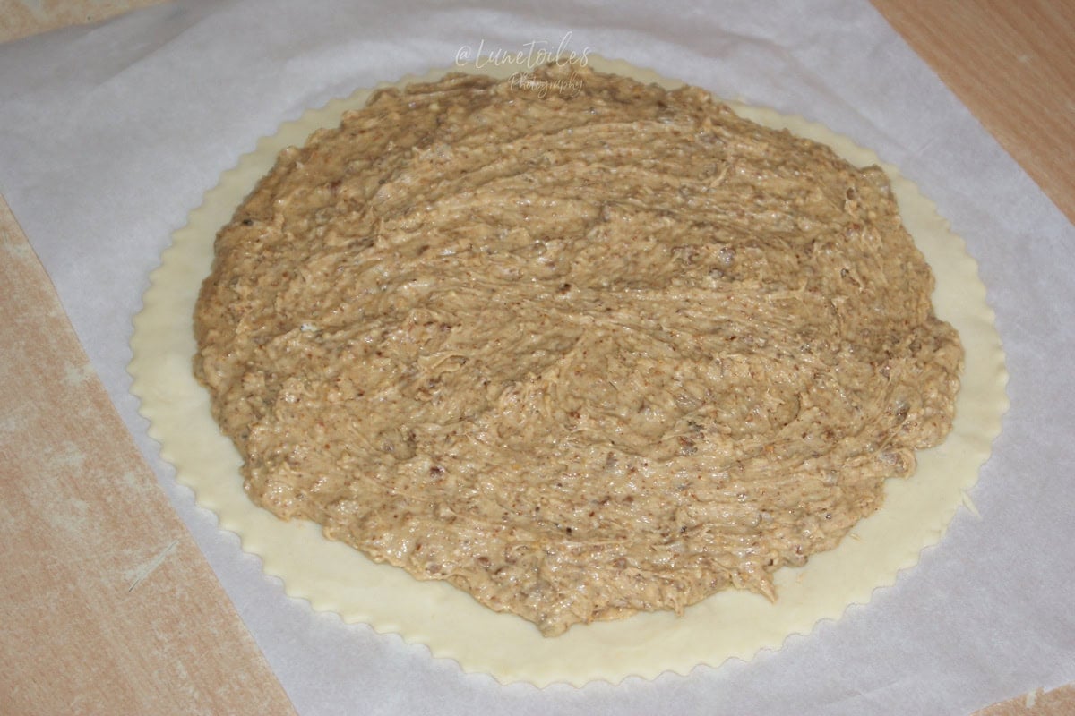 Disque de pâte feuilletée posé sur papier cuisson, recouvert d’une couche de frangipane à la noisette (crème de noisettes) étalée en cercle, prêt à être refermé pour une galette.