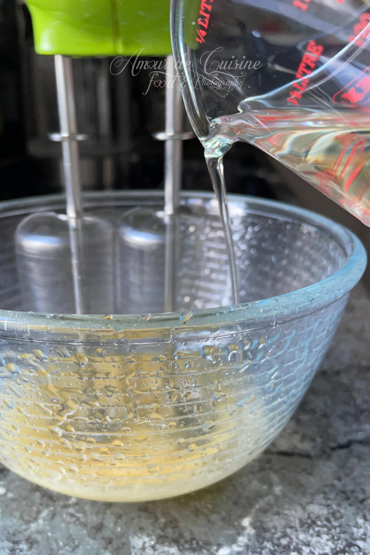 Huile versée en filet dans un bol en verre avec batteur électrique pour monter une mayonnaise maison, étape de l’émulsion en cours, photo Amour de Cuisine.