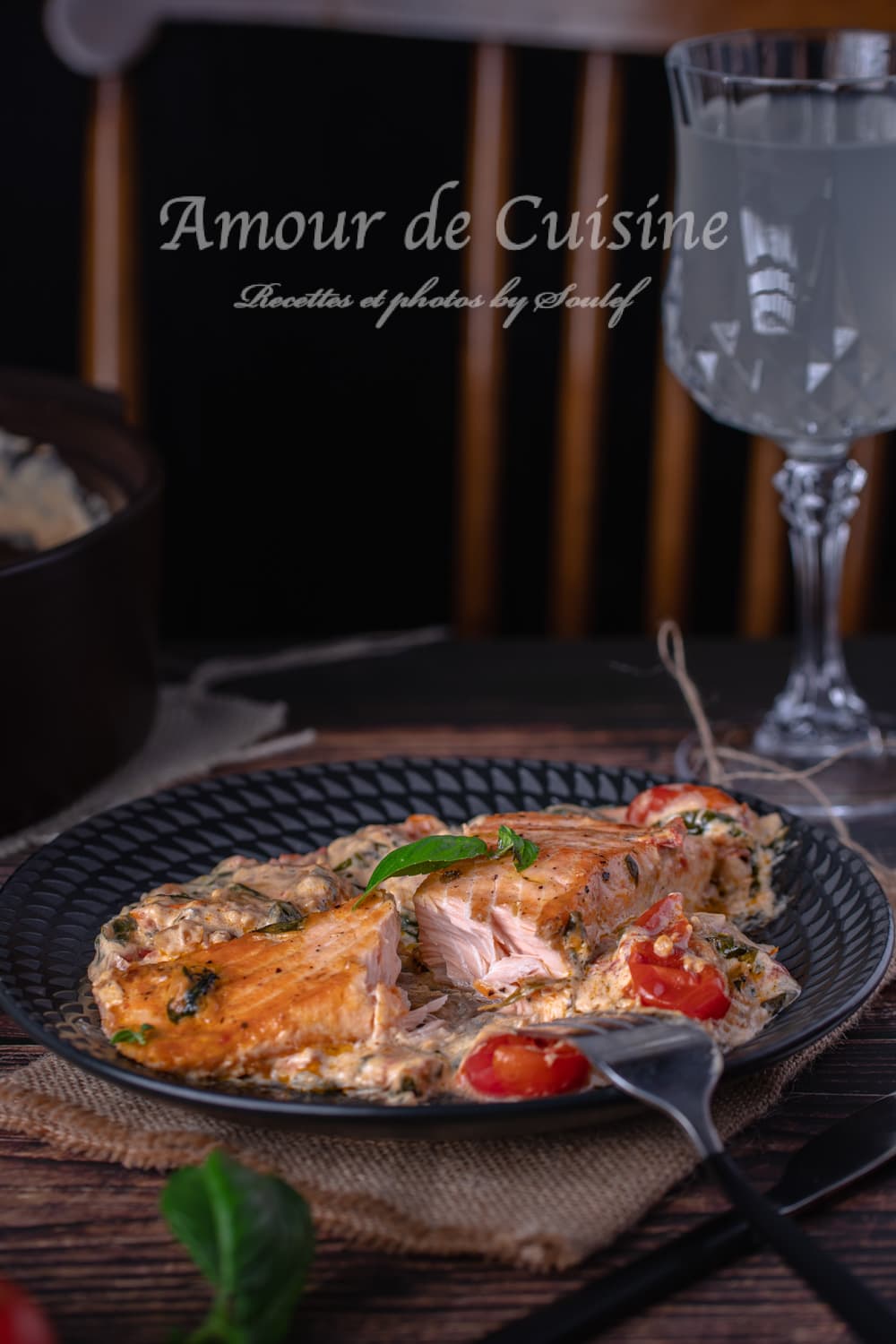 Flaky Tuscan salmon served on a black plate with creamy spinach sauce, cherry tomatoes, and basil, accompanied by a glass of lemonade on a rustic wooden table.