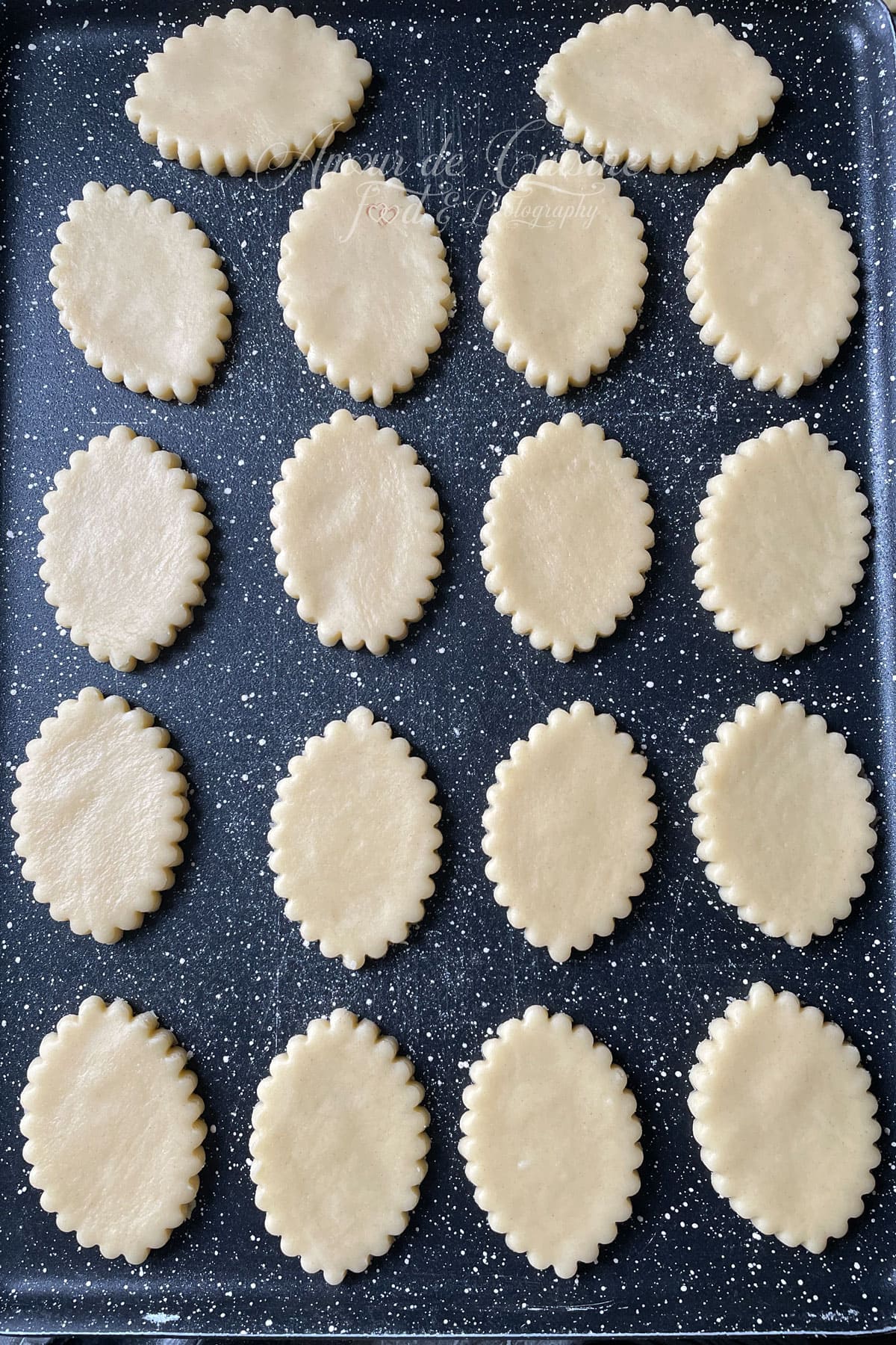 Biscuits sablés découpés crus sur plaque de cuisson, prêts à être enfournés pour préparer des sablés à la confiture maison.