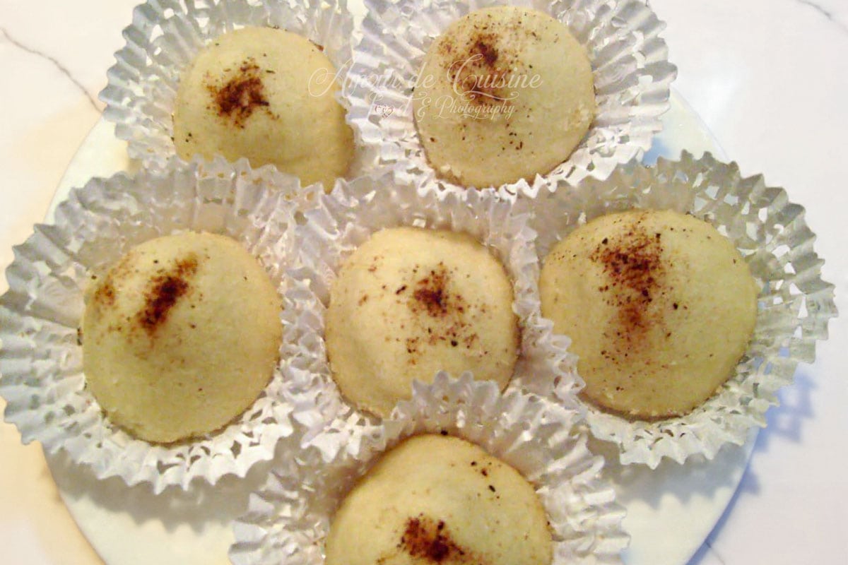 Montecaos maison fondants saupoudrés de cannelle, disposés dans des caissettes blanches sur une assiette.