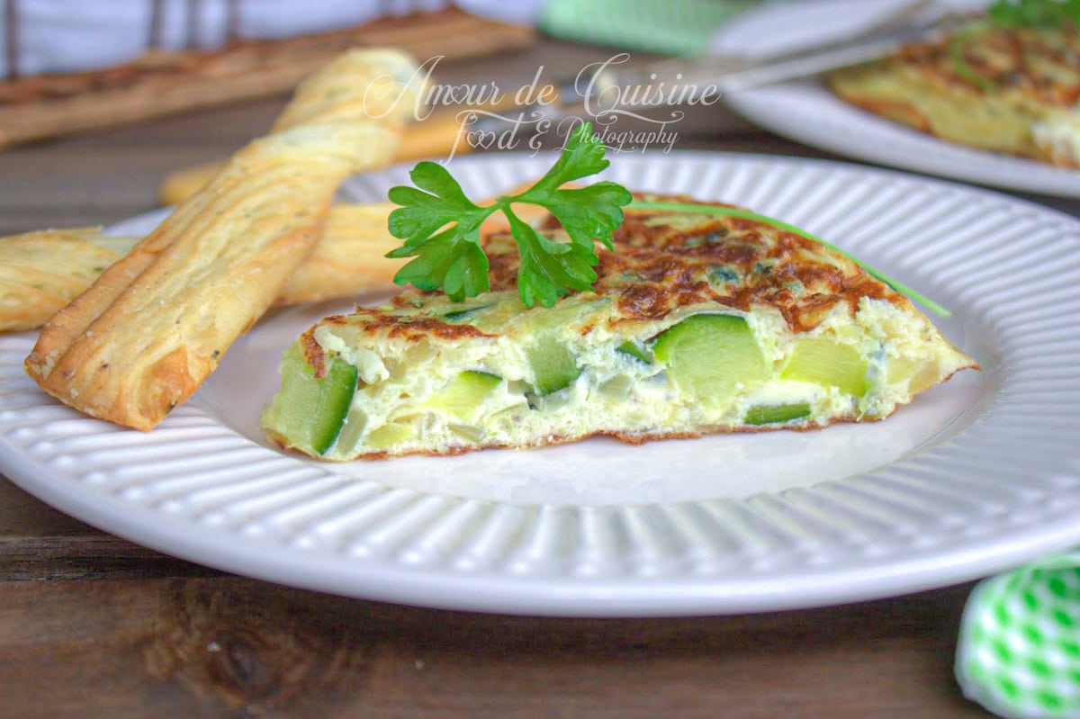 Part d’omelette espagnole aux courgettes garnie de persil frais, servie sur une assiette avec des gressins feuilletés – photo gourmande signée Amour de Cuisine