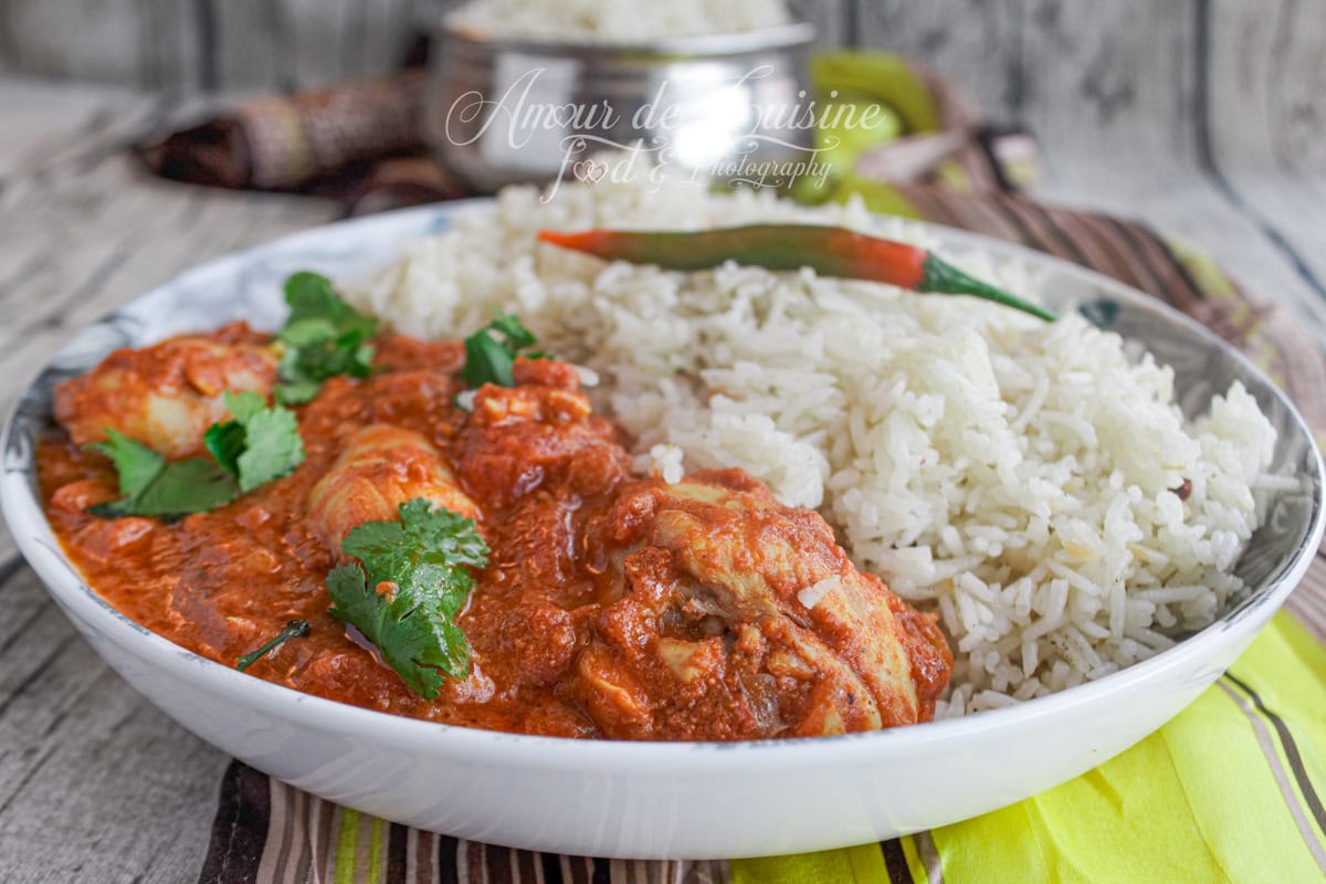Chicken tikka masala in a rich red creamy sauce served with white basmati rice, garnished with fresh coriander and a red chili pepper, presented on a white plate