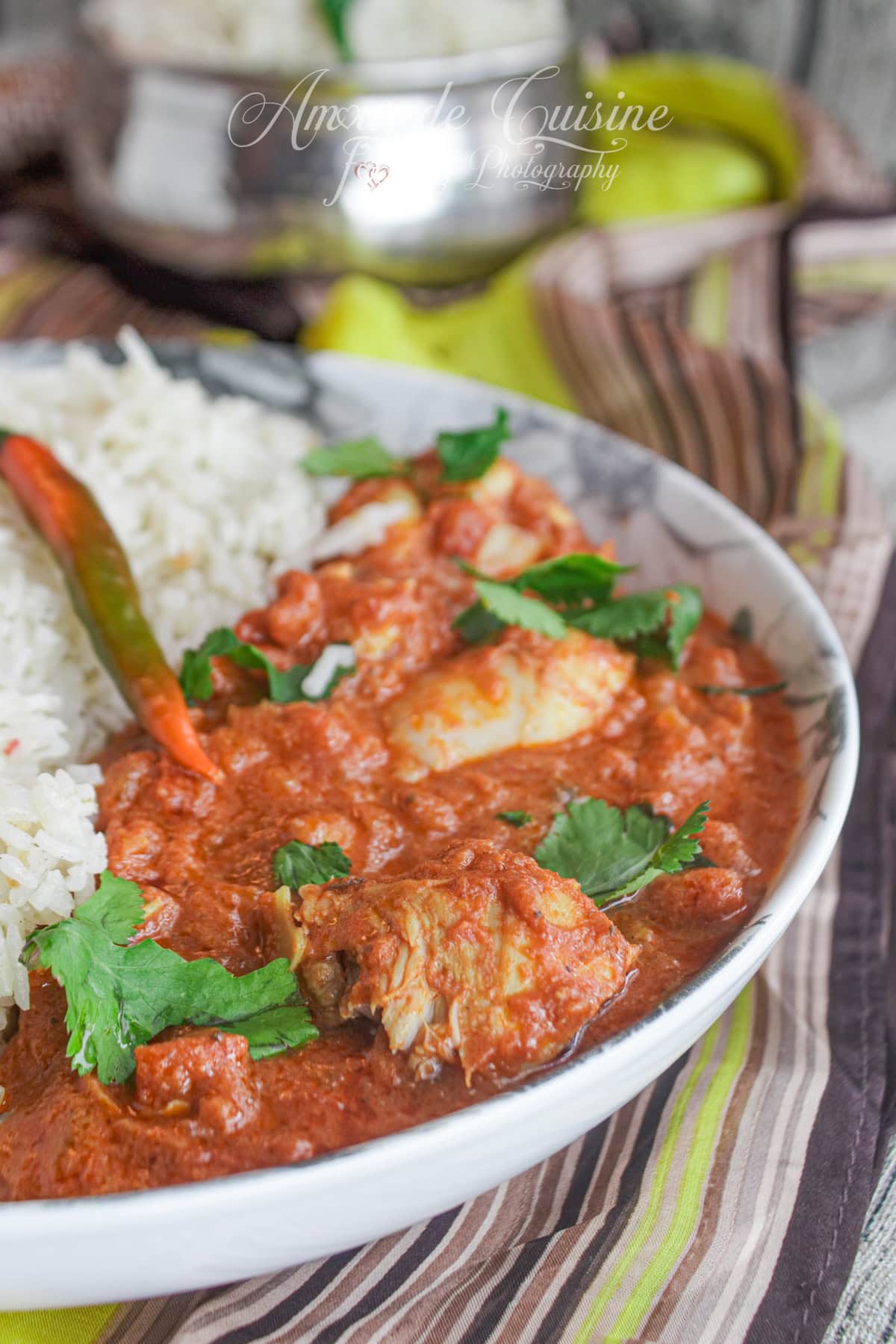 Plate of creamy chicken tikka masala served with basmati rice, garnished with fresh coriander and a chili pepper, close-up of a spicy Indian dish