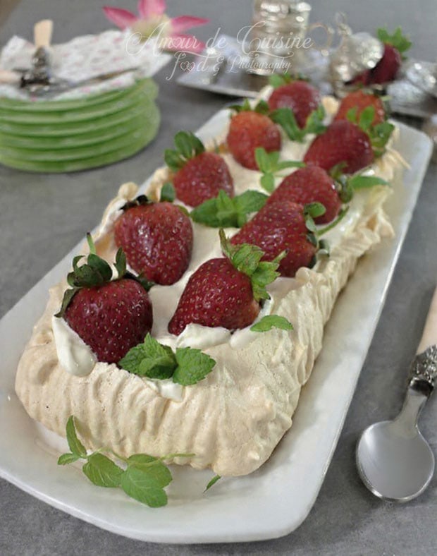 Homemade rectangular pavlova topped with whipped cream, whole strawberries, and mint leaves, presented on a white serving dish.