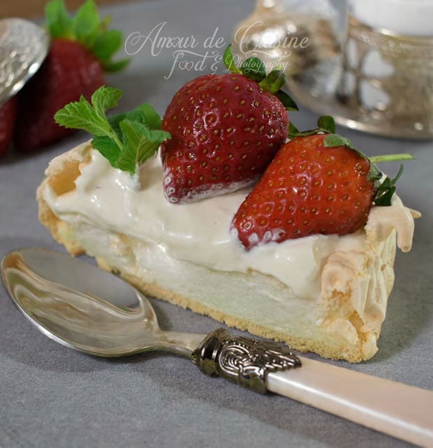 Slice of pavlova topped with smooth whipped cream, fresh strawberries, and mint leaves, served with a vintage spoon on a tabletop.