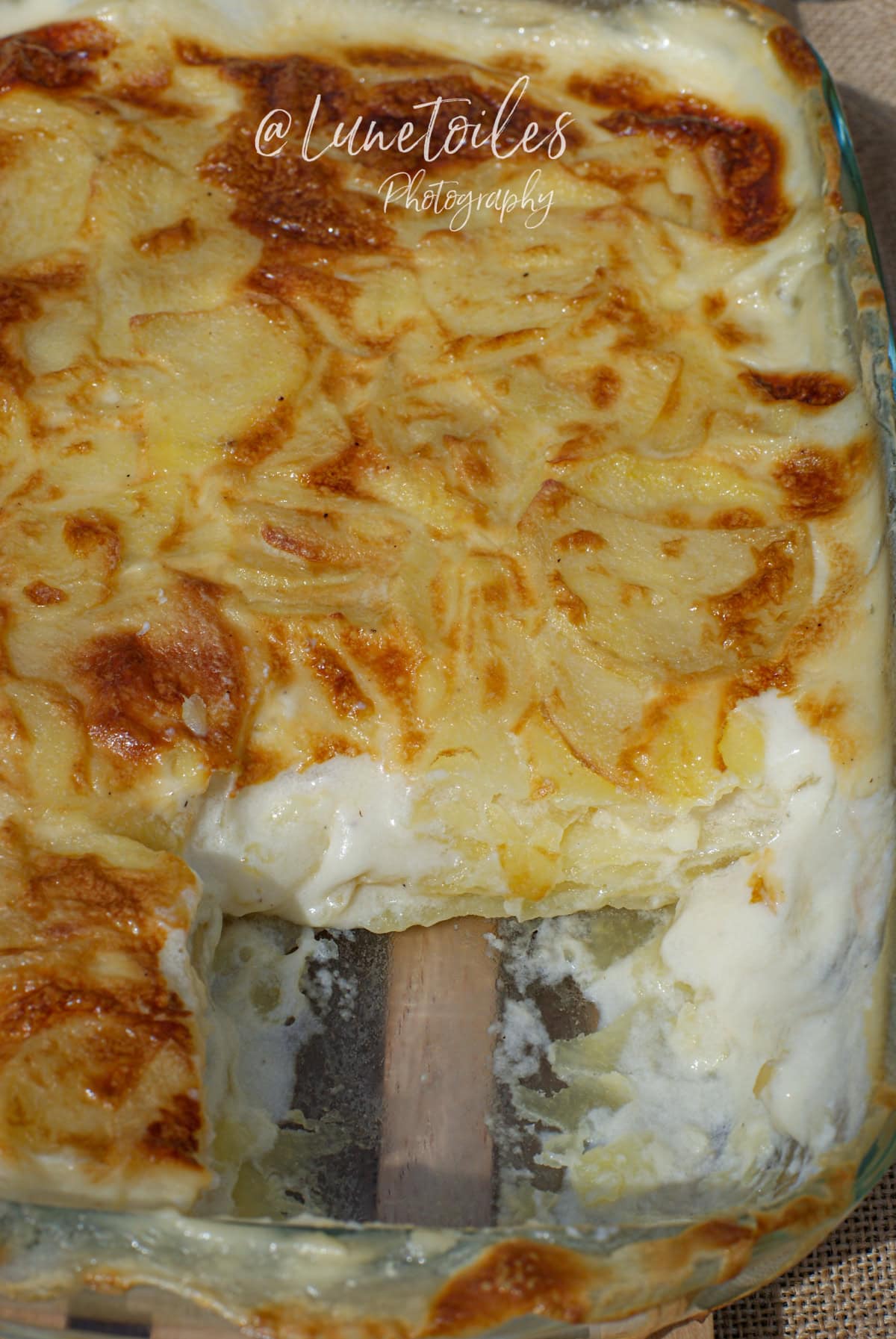 Gratin dauphinois maison entamé, à la texture fondante et crémeuse, avec une surface dorée et des lamelles de pommes de terre visibles, dans un plat en verre