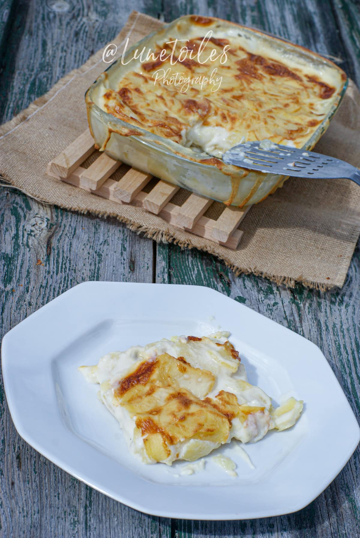 Gratin dauphinois maison crémeux et doré, servi dans un plat en verre sur une planche en bois, avec une portion dressée à l’assiette sur une table rustique en bois vieilli