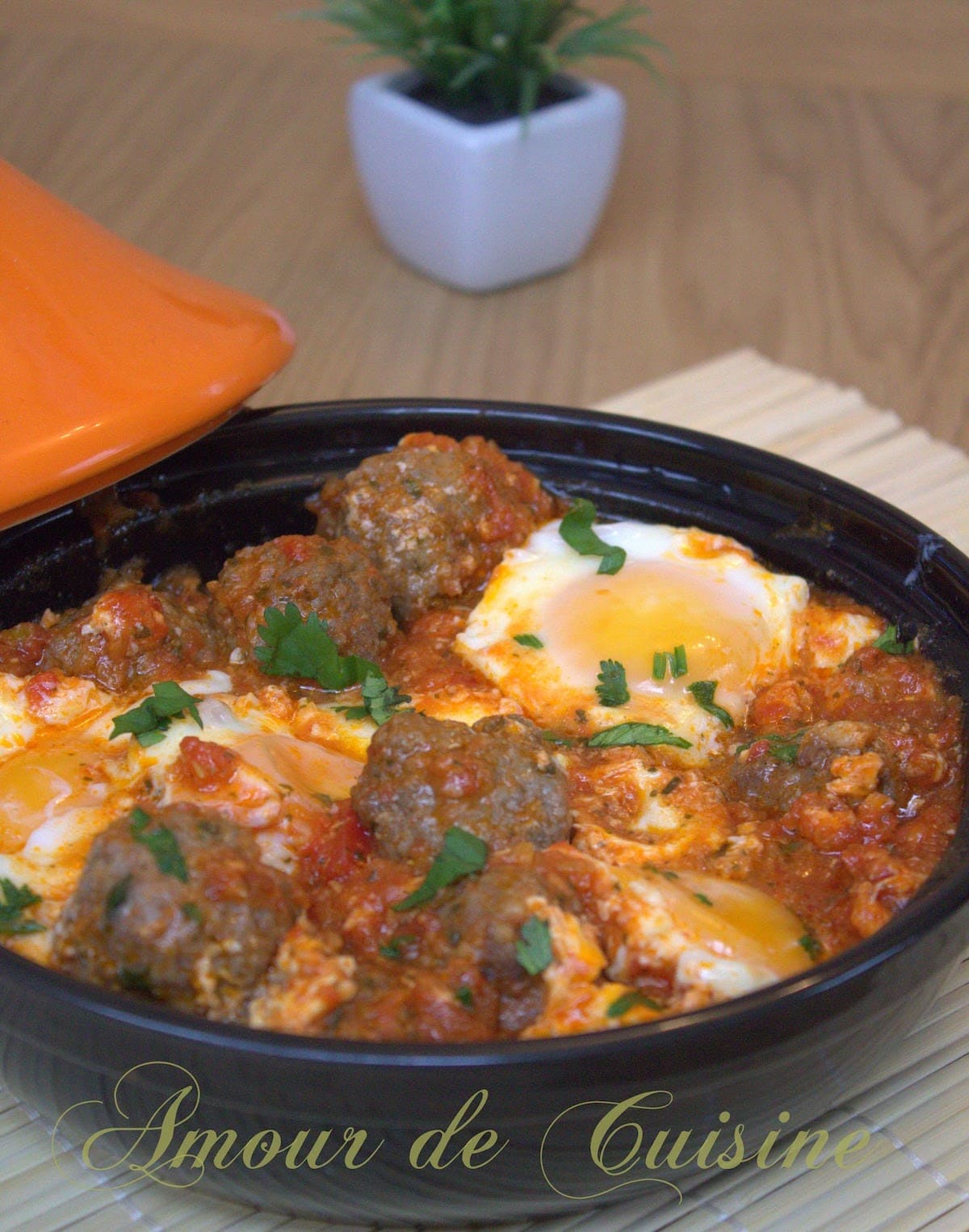 Moroccan kefta and eggs tagine in a clay dish: meatballs simmered in spiced tomato sauce, eggs set with slightly runny yolks, topped with fresh parsley.