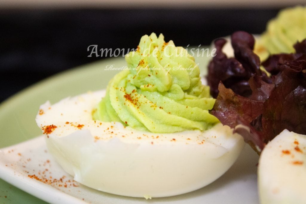 Deviled egg topped with a smooth avocado cream, beautifully piped and sprinkled with paprika, served on a plate with fresh salad leaves.