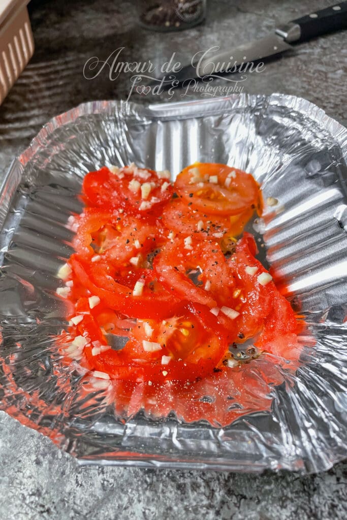 Rondelles de tomates et ail assaisonnés dans une barquette avant cuisson du saumon au Airfryer.