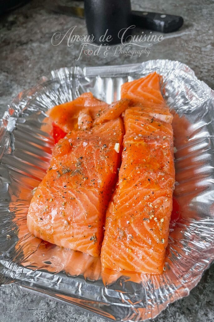 Morceaux de saumon assaisonnés posés sur un lit de tomates et d’ail avant cuisson au Airfryer.
