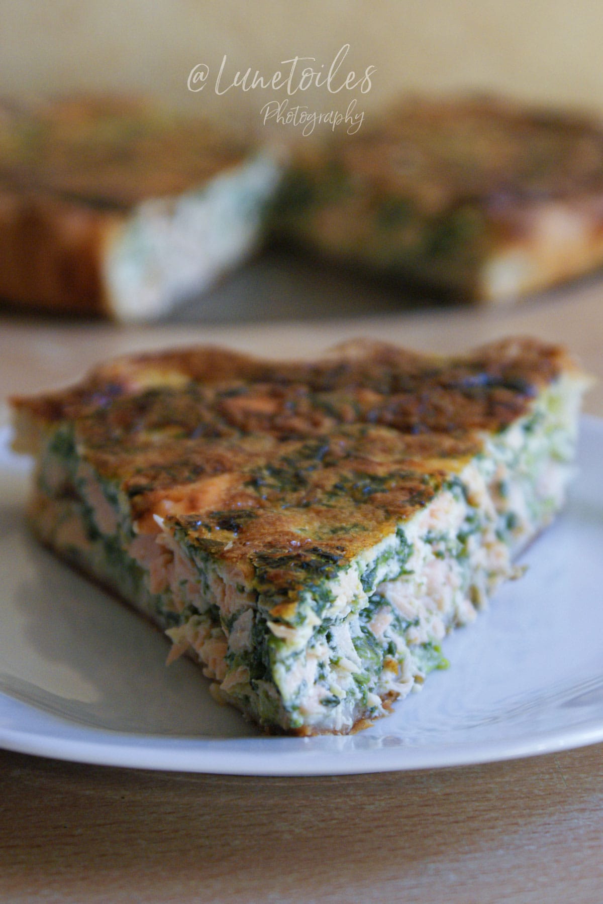 Part de quiche saumon épinard servie sur une assiette blanche, avec texture moelleuse et garniture fondante