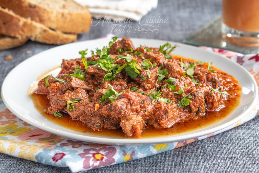 Close-up of kebda mchermla (lamb liver in spicy tomato sauce) topped with fresh coriander, with slices of homemade bread in the background.