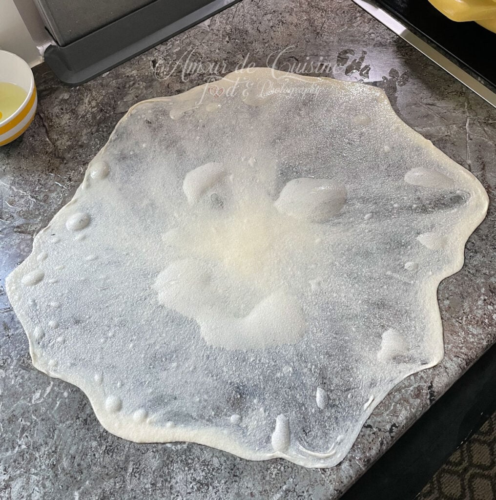 Pâte à msemen étirée très finement sur un plan de travail huilé, presque transparente, avant le pliage en crêpe feuilletée.