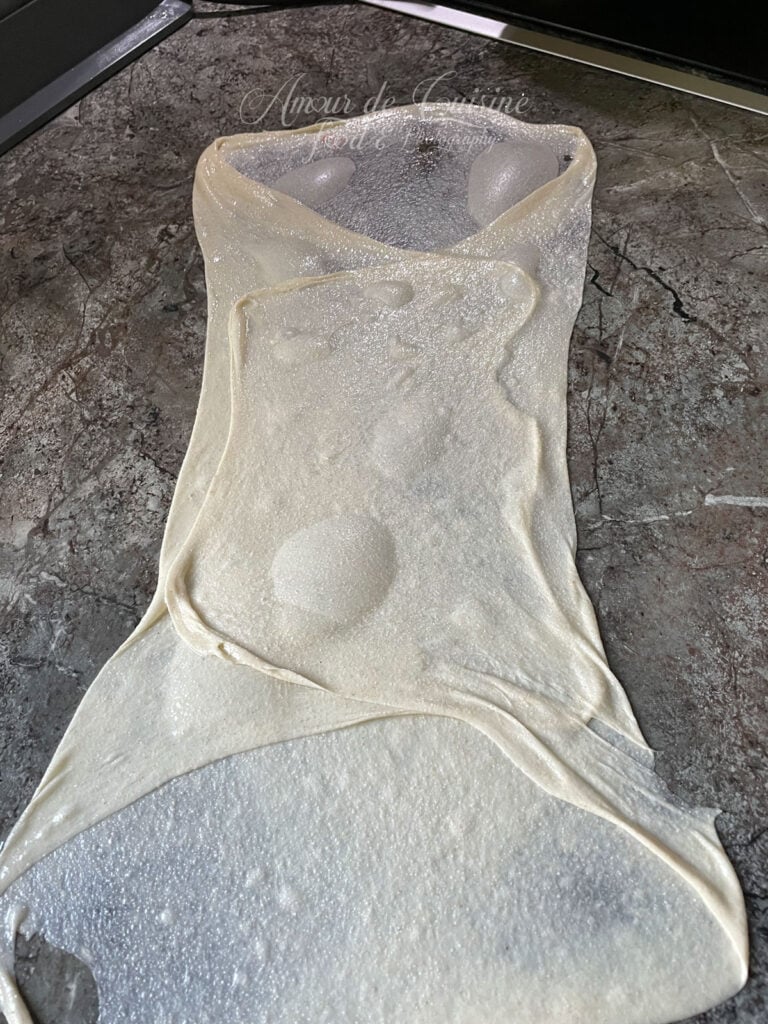 Pâte à msemen très fine en cours de pliage sur un plan de travail huilé pour former les couches feuilletées.