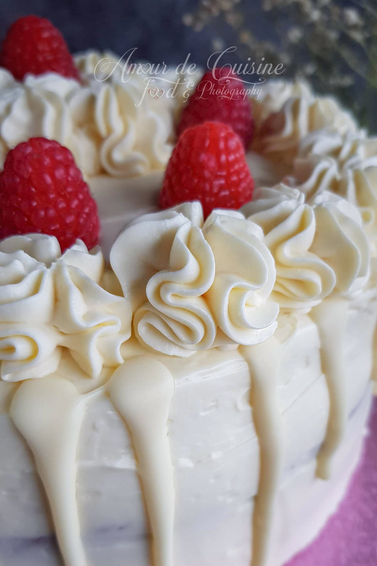 Layer cake recouvert de ganache montée chocolat blanc et mascarpone, décoré de rosaces à la douille, framboises fraîches et drip de chocolat blanc.