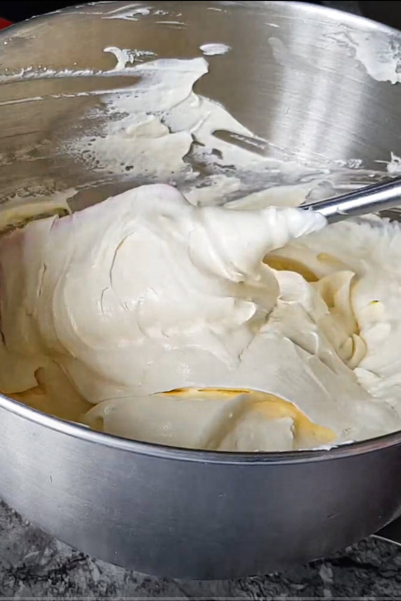 Ganache montée chocolat blanc et mascarpone dans un bol en inox, texture épaisse et lisse, prête à être pochée à la spatule.