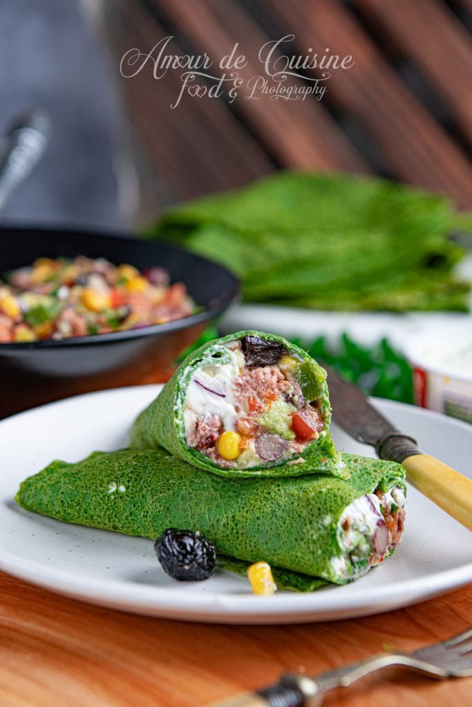 Deux wraps d’épinards garnis de salade mexicaine au thon, coupés en biais et présentés sur une assiette blanche, révélant une farce colorée à base de maïs, haricots, tomates, olives noires et fromage frais, avec un fond de galettes vertes empilées