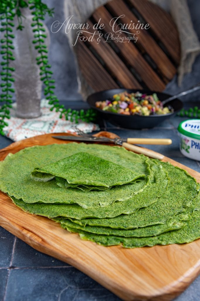 Tortillas vertes aux épinards sans gluten, joliment empilées sur une planche en bois, prêtes à être servies avec une salade colorée de légumes dans un bol en arrière-plan