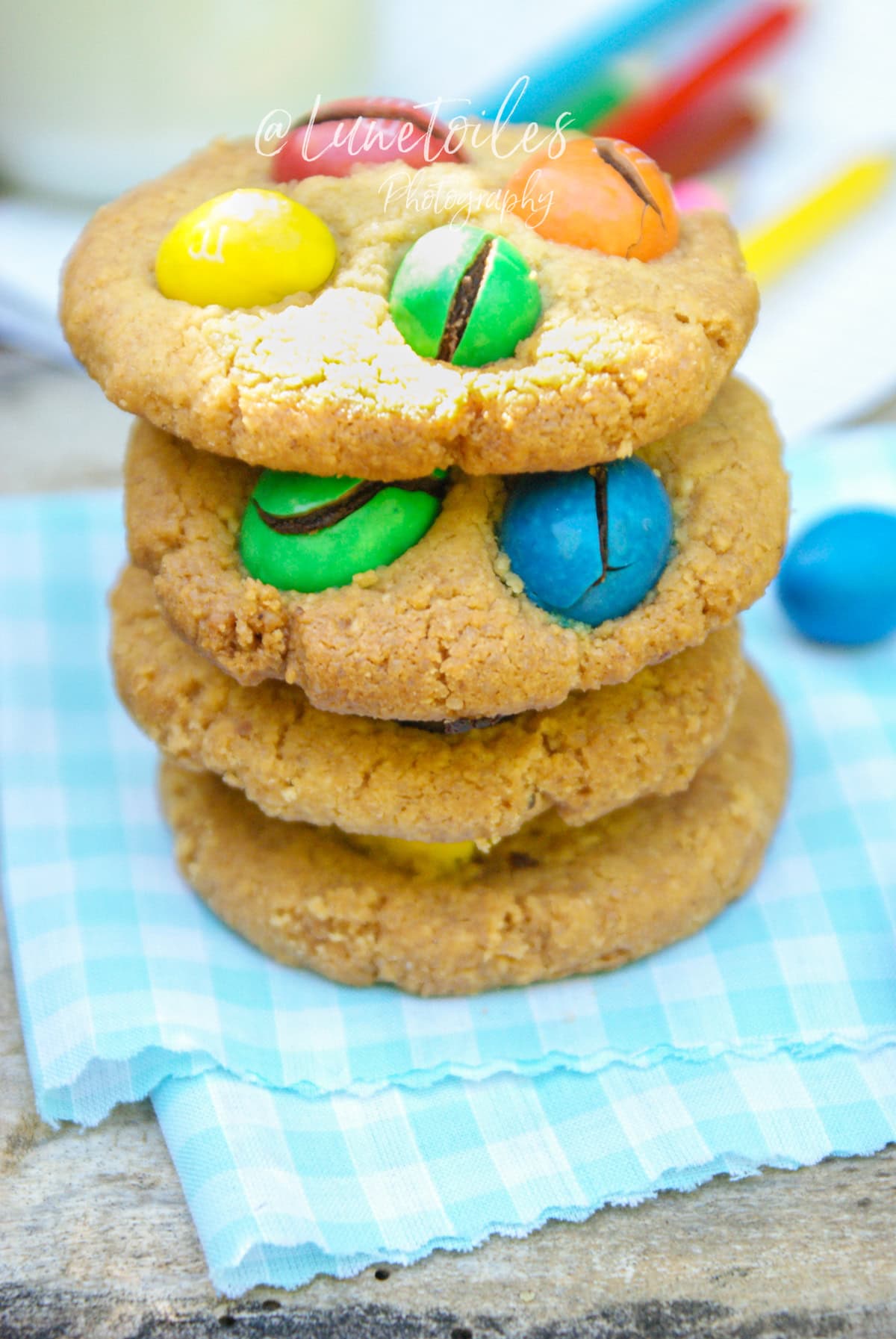 Cookies maison aux M&M’s colorés empilés sur une serviette à carreaux bleus, moelleux et dorés, parfaits pour un goûter fait maison – recette de Lunetoiles