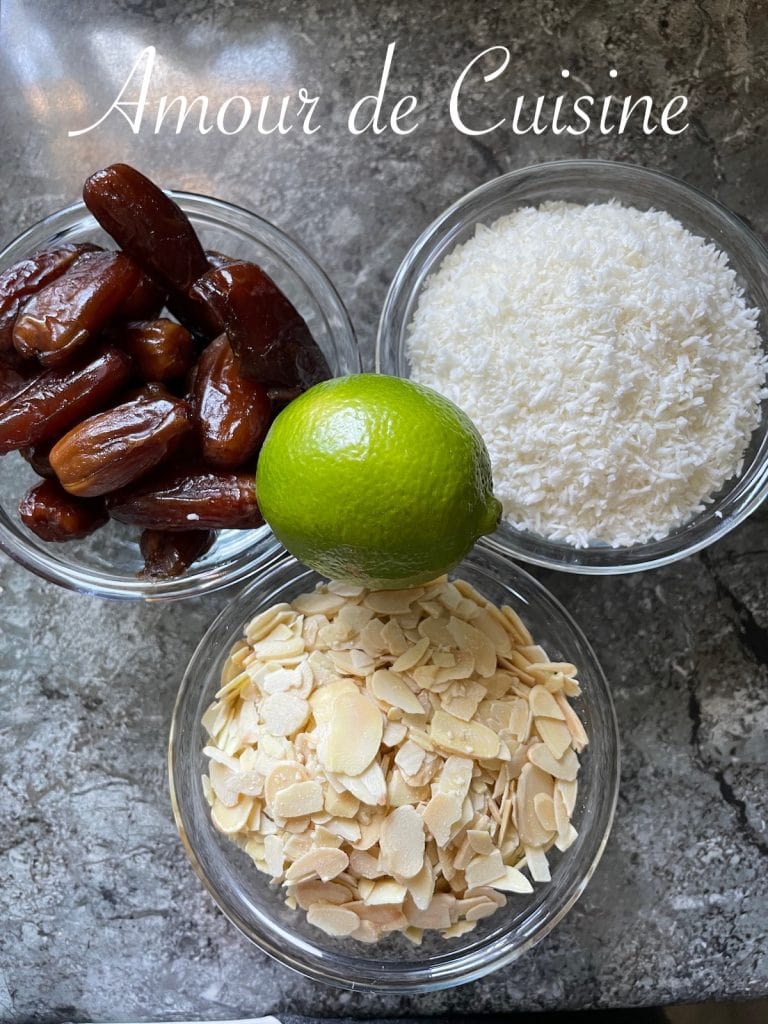 Close-up of pitted dates, shredded coconut, almonds, and lime in glass bowls on a stone background