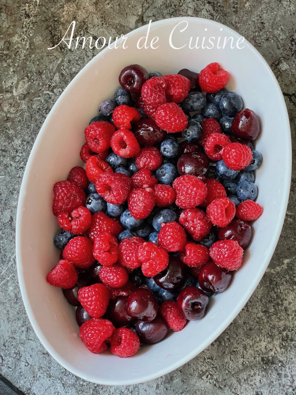 Mélange de fruits rouges dans un plat blanc : framboises, myrtilles et cerises, prêts à être utilisés pour un dessert frais ou une terrine fruitée