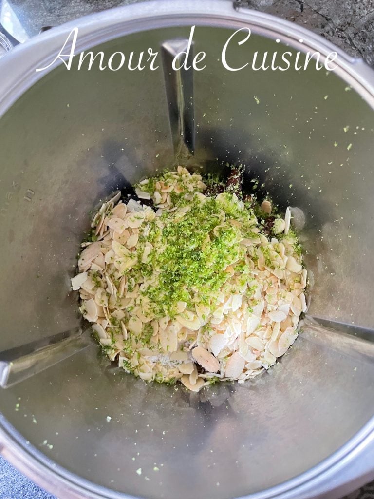 Raw ingredients in a food processor: sliced almonds, dates, shredded coconut, and lime zest