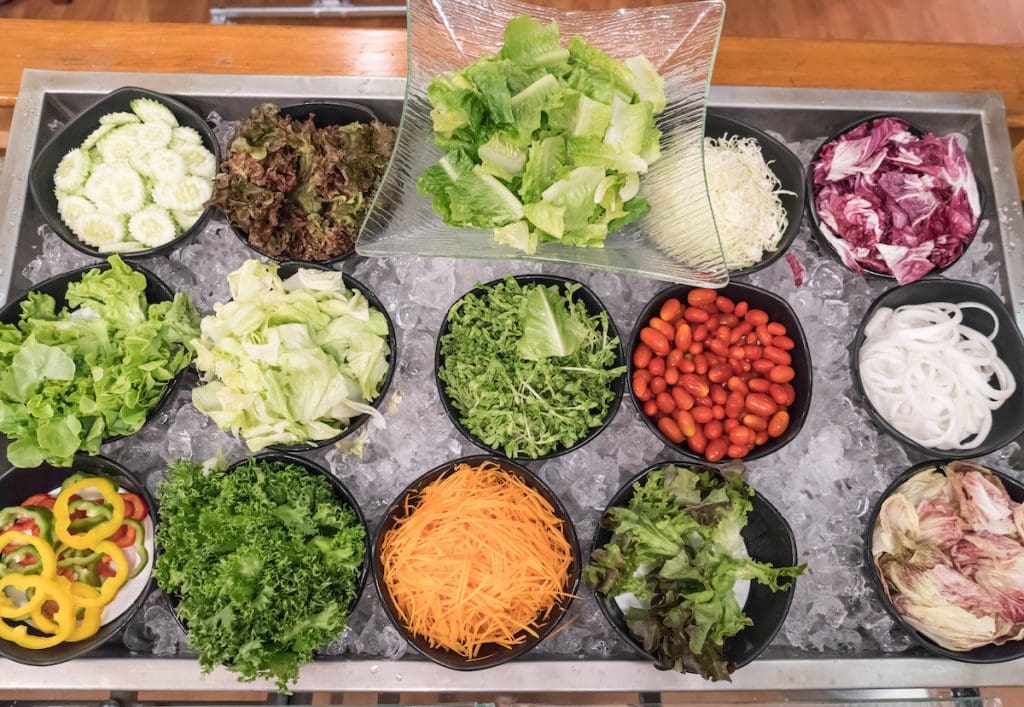 Saladette ou Buffet de salade fraîche composé de légumes variés comme carottes râpées, tomates cerises, concombres, oignons, poivrons, laitues et jeunes pousses, présentés sur lit de glace dans une saladette réfrigérée, idéal pour une conservation optimale lors d’un buffet ou d’un événement en plein air.