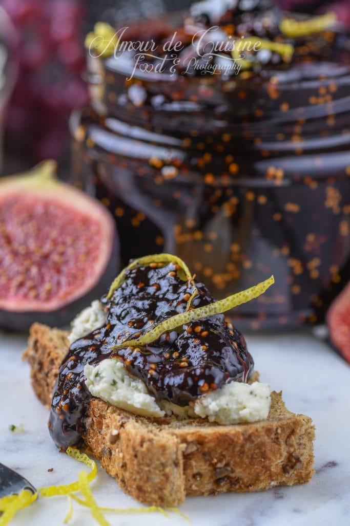 Toast de pain aux céréales garni de fromage crémeux et de confit de figues au vinaigre balsamique, décoré de zestes de citron, avec figues fraîches en arrière-plan