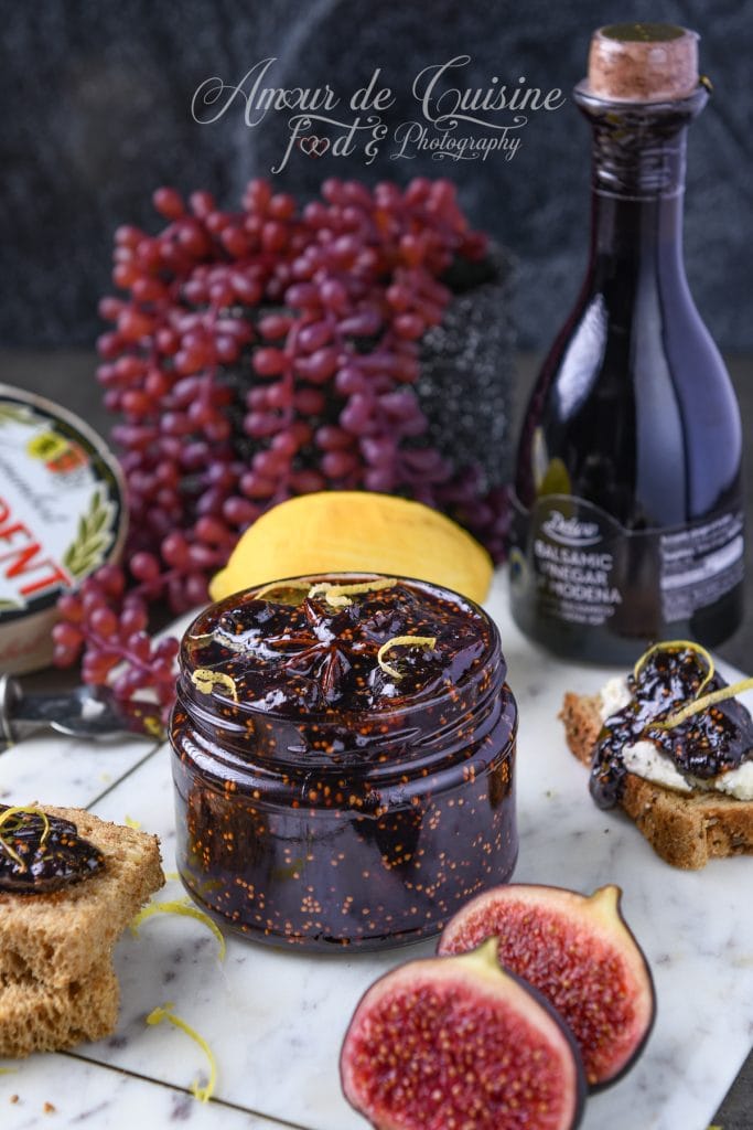 Bocal de confit de figues au vinaigre balsamique maison, décoré de zestes de citron, entouré de figues fraîches, de pain grillé et d’une bouteille de vinaigre balsamique