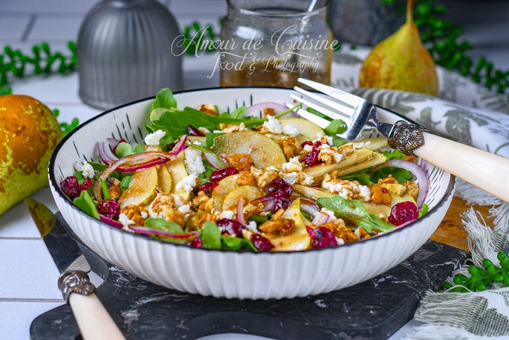 Bol de salade aux poires, roquette, noix de pécan grillées, cranberries séchées et feta émiettée, servi avec une vinaigrette balsamique-érable maison, accompagné d’une fourchette élégante sur une table rustique.